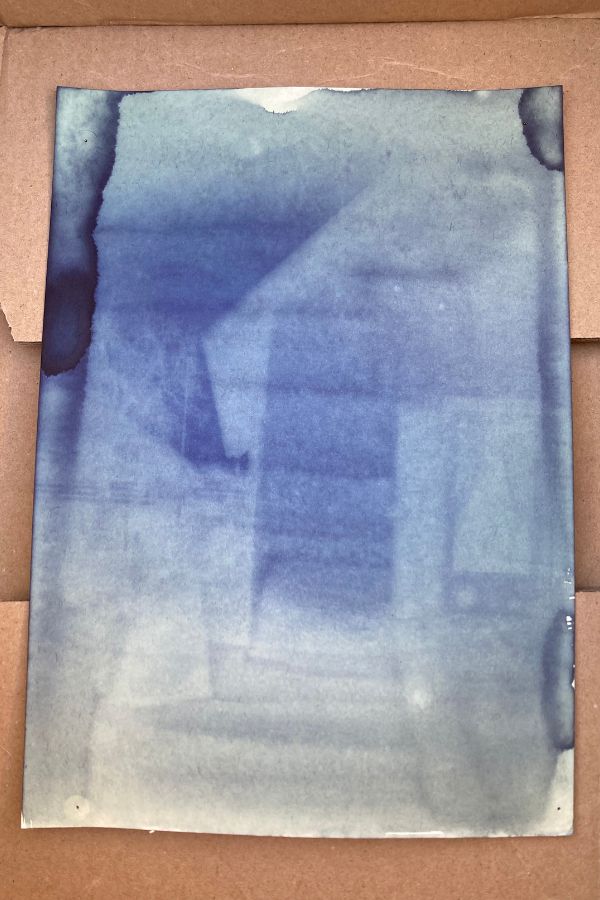ein Din A4 Blatt zeigt ein Cyanotypie-Negativ in abgestuften Blautönen. Es ist ein Haus mit Dach und Terassentür zu erkennen.
