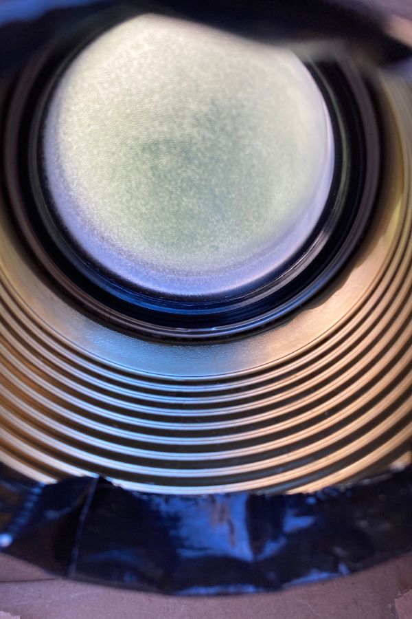 Eine Linse sitzt am gegenüberliegenden Ende einer Konservendose (Blick von innen). Sie ist beschlagen/vereist.